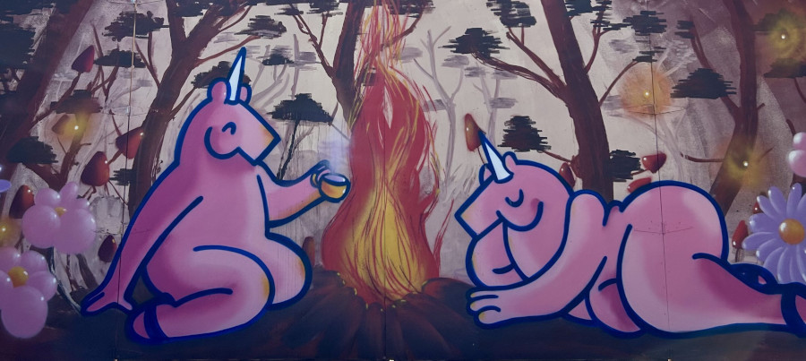 Photo of graffiti depicting two pink unicorns relaxing in a forest near a campfire. Post cover